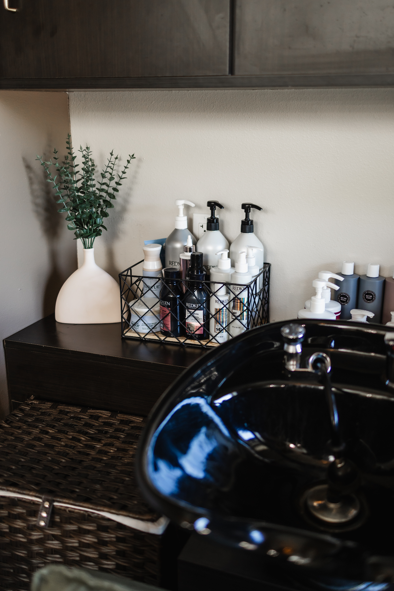 Salon products and haircare treatments arranged on a dark counter with a shampoo bowl at Jenna Lauren Hair Designs